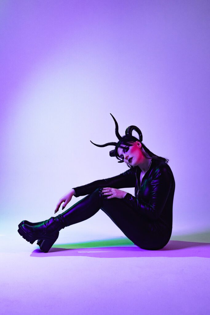 Unique studio portrait of a model in a black bodysuit and horned headpiece bathed in purple lighting, captured by a Portland creative portrait photographer.
