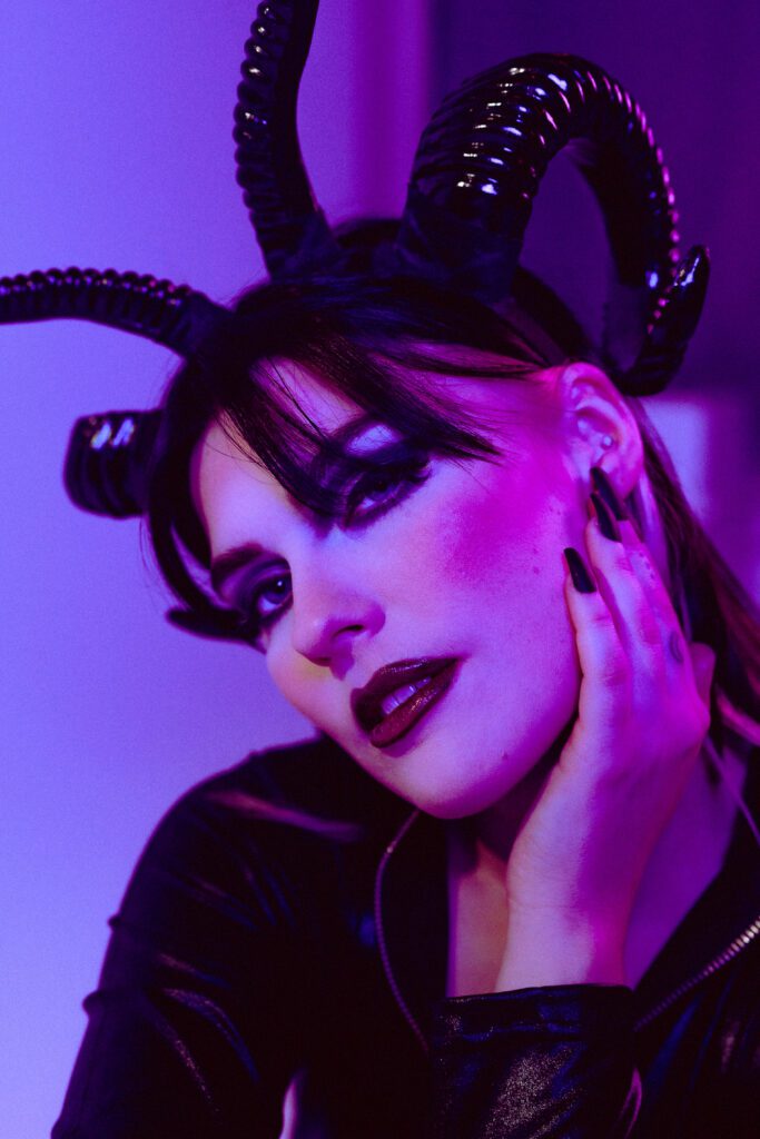 Dark glam portrait of woman in black horns and dramatic makeup, bathed in purple gel lighting during a conceptual creative session in The Studio Lab