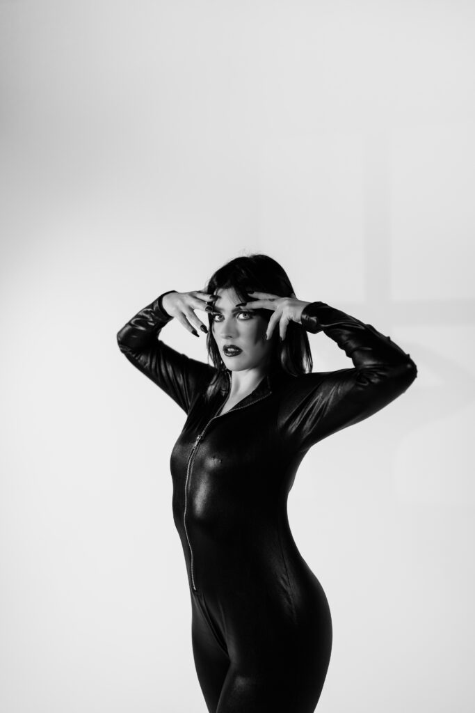 Powerful full-body black-and-white portrait of a woman in sleek catsuit, posing confidently in minimal lighting—shot during a monochrome Studio Lab concept by Mewphotovideo