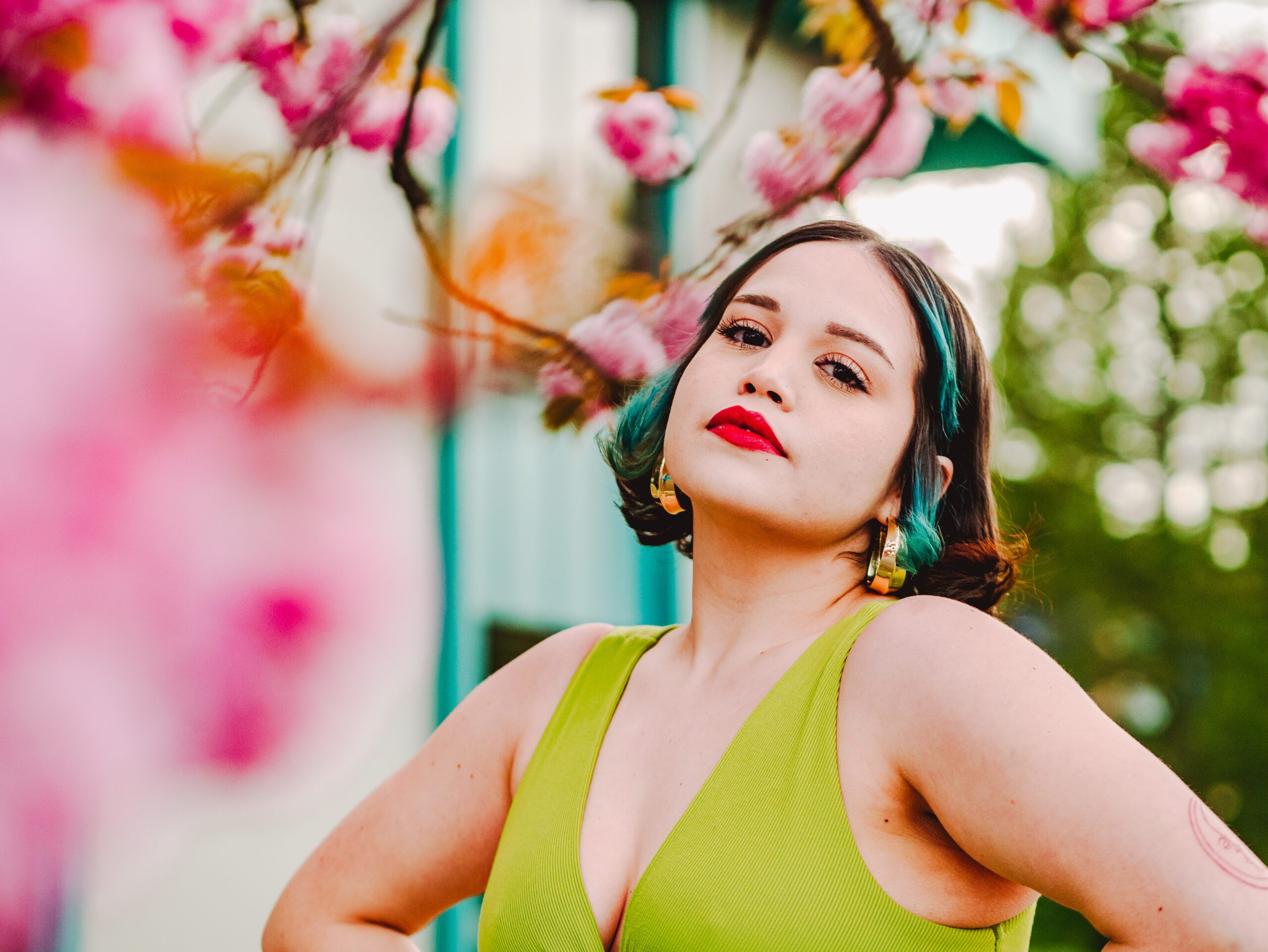 Bold editorial portrait of a woman in a green dress framed by soft pink blossoms during a vibrant spring Outdoor Adventure session in Portland, Oregon