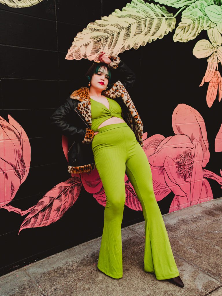 Stylish woman in bright green pantsuit standing powerfully in front of a floral mural wall during an expressive Outdoor Adventure brand session in Portland, Oregon