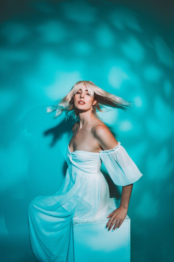 Soft, ethereal brand photo of woman in white blouse and pants lit by teal tones, blending modernity and softness during a creative Studio Lab session