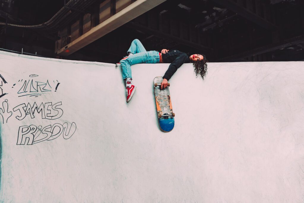 Client reclining on the edge of a graffiti-covered skate ramp holding a skateboard, wearing bold red sneakers and denim—part of an urban Outdoor Adventure brand photography session in Portland, Oregon