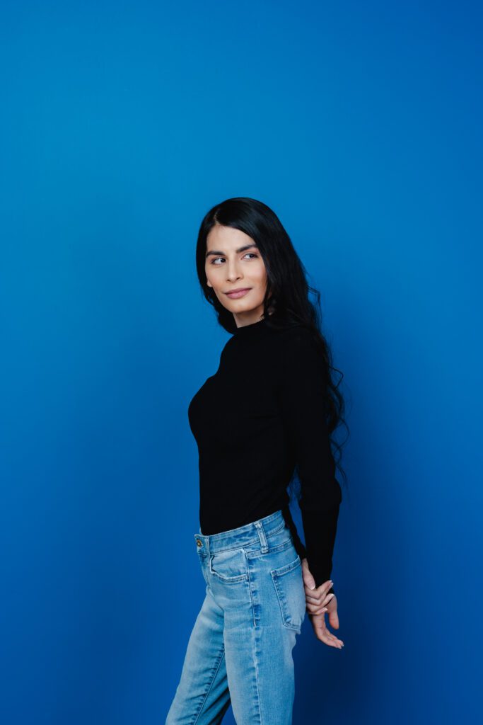 Portrait against a bold blue backdrop with a black top and jeans, highlighting confident posing for creatives.