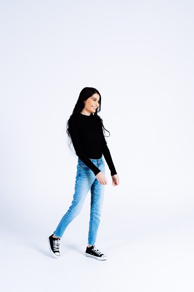 Candid walking shot against a white background with a black top and jeans—great for creative portraits.