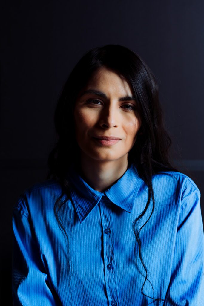 Studio headshot in deep shadows and rich blue tones, emphasizing confidence and professionalism.