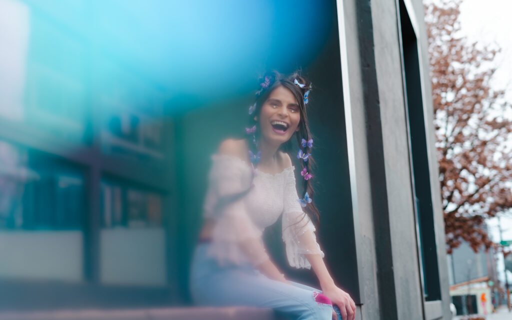 Creative outdoor brand photo of a woman laughing with butterflies in her hair, captured through a soft blue light overlay—perfect for unconventional personal branding in Portland.