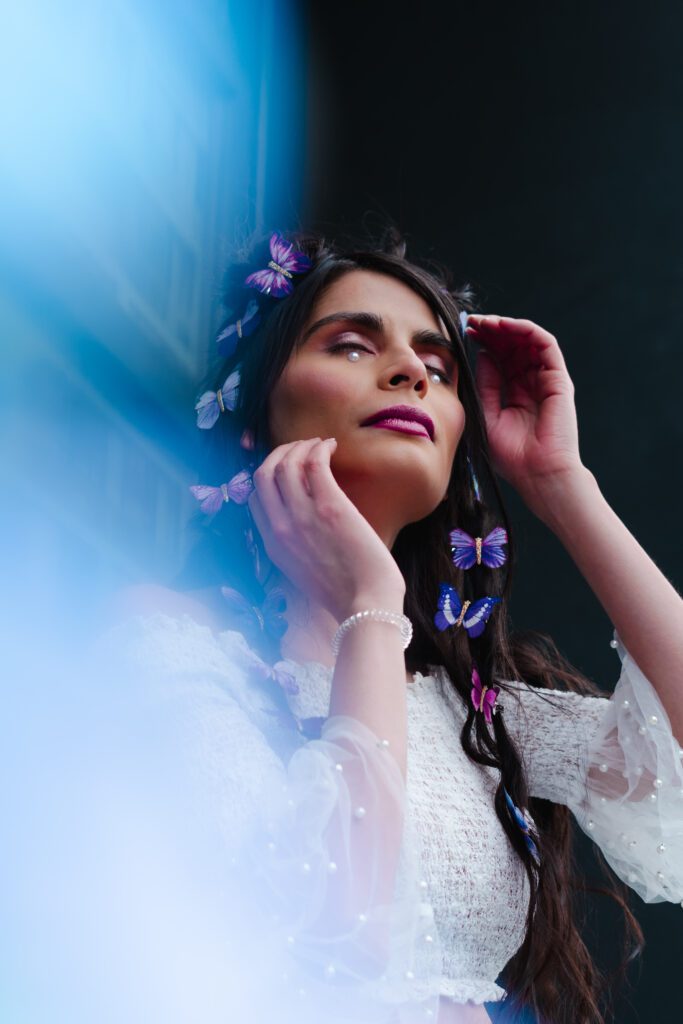 Moody pastel brand photo with ethereal blue wash, showing a creative woman in butterfly glam styling during an outdoor Portland editorial shoot.