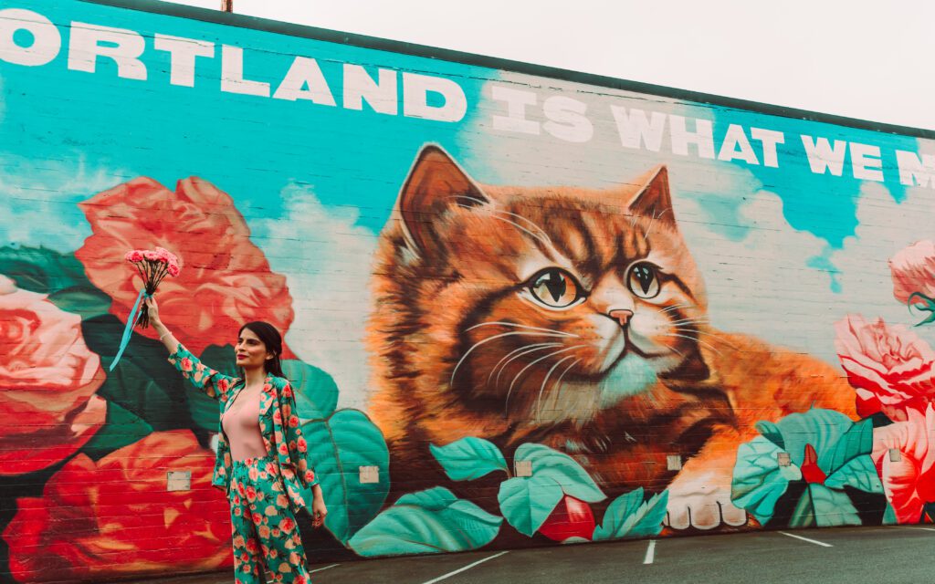 Editorial-style branding photo of a woman in a matching floral outfit holding flowers in front of the “Keep Portland Weird” cat mural—captured for a vibrant, personality-driven photo session in Portland, Oregon.