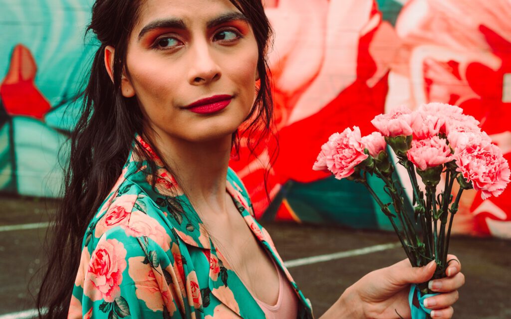 Candid creative brand portrait with intense gaze and bouquet of pink carnations.