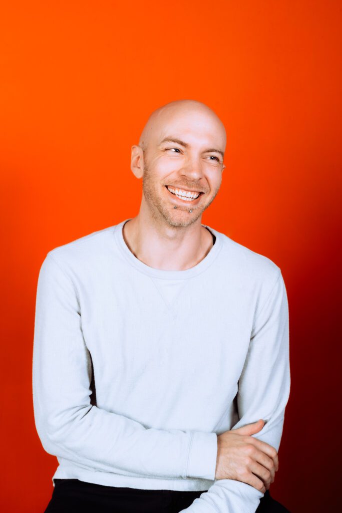 Professional headshot with a relaxed smile and bright orange background, part of a modern branding shoot in The Studio Lab