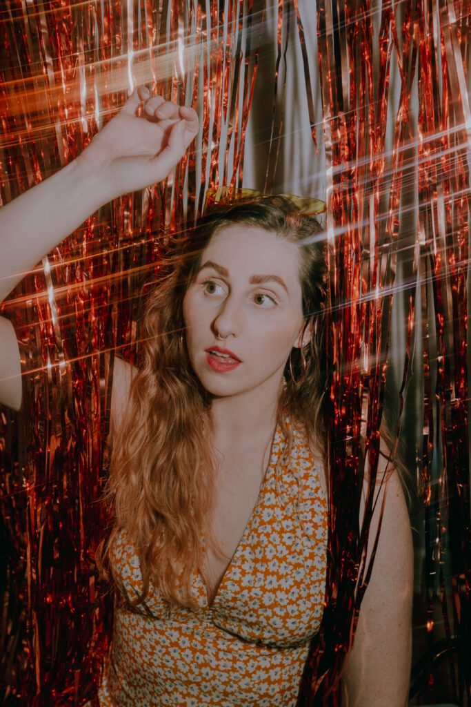 Close-up portrait of client surrounded by red foil strands with soft bounce lighting, part of a styled branding shoot in The Studio Lab by Mewphotovideo