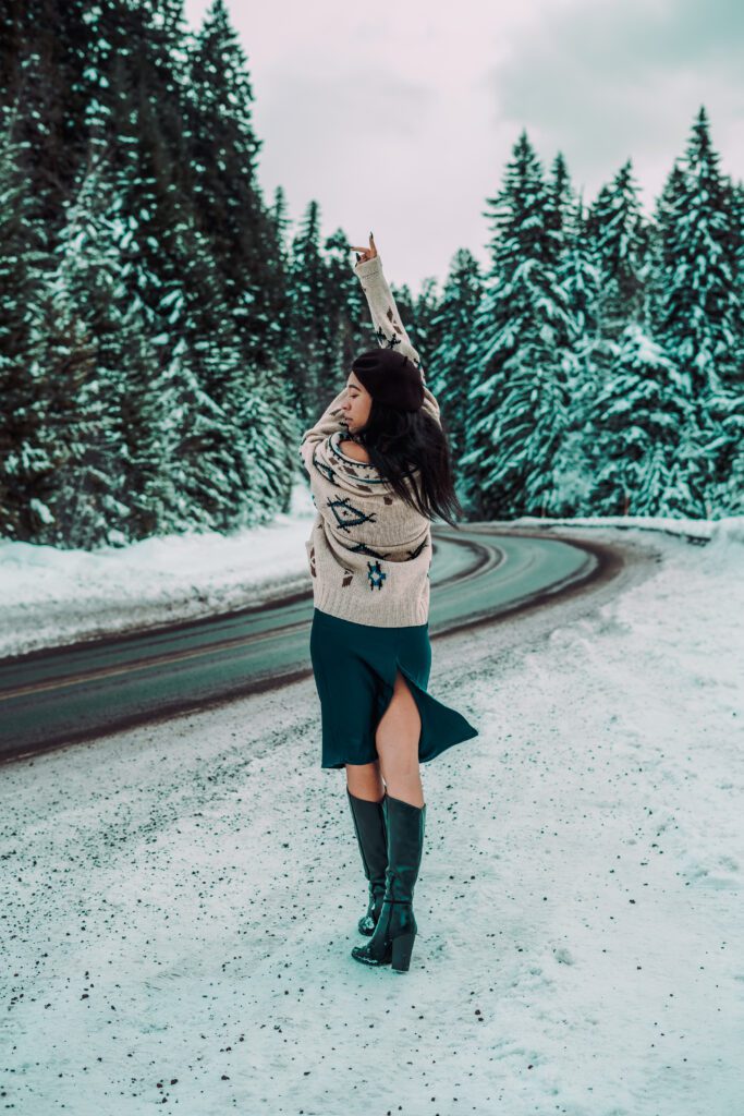 Woman in boots and winter styling standing on snowy road under dramatic sky, photographed during a cinematic winter Outdoor Adventure session