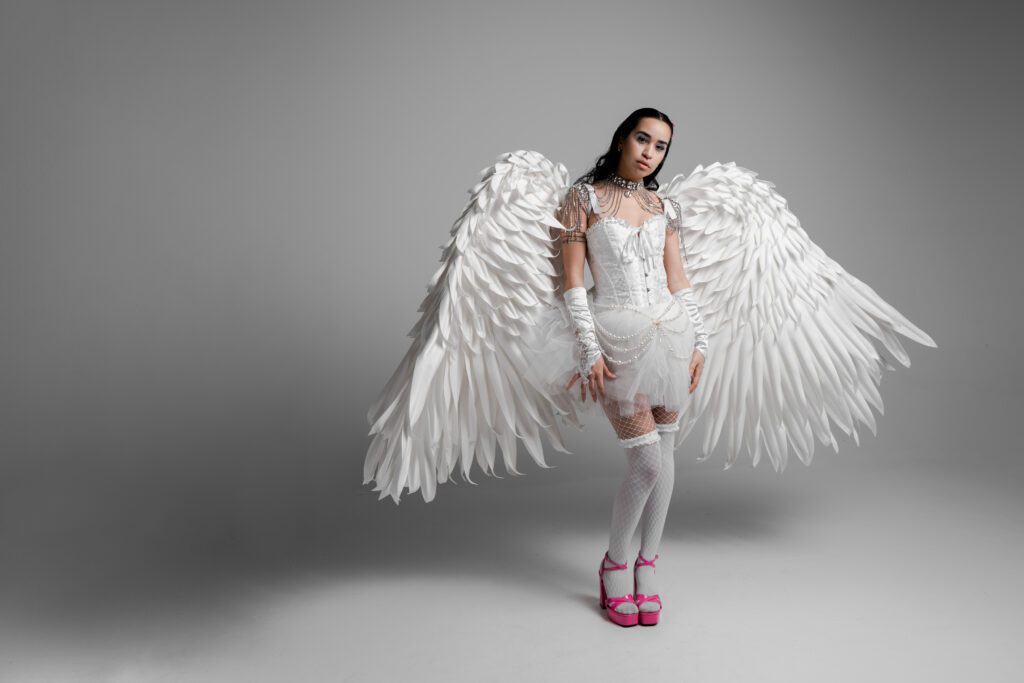 Full-body studio portrait of woman with dramatic white angel wings and hot pink heels, captured in a monochrome creative shoot by a Portland brand photographer