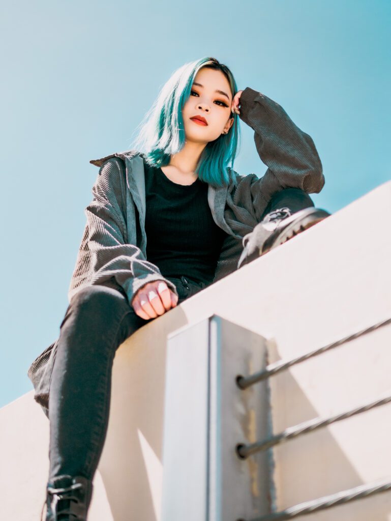 Client with blue hair perched on a rooftop ledge, gazing into sunlight—captured during a relaxed, vibrant Outdoor Adventure urban shoot in Portland, Oregon
