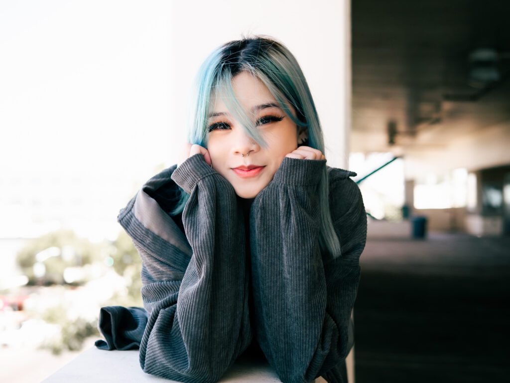 Close-up urban portrait of woman with blue hair and cozy sweater, smiling softly in shaded natural light—part of an Outdoor Adventure session for creatives