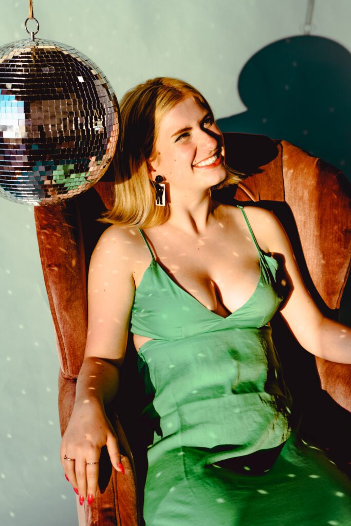 Client in green satin dress seated under a disco ball, bathed in light play and sparkle—part of a playful, glam concept inside The Studio Lab