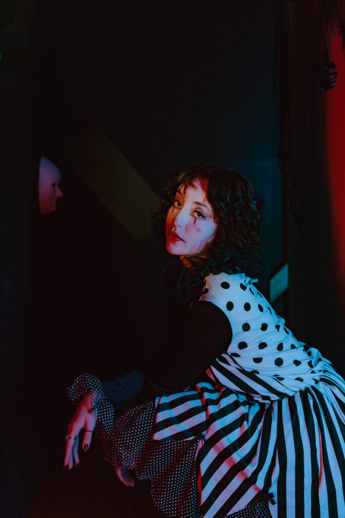 Cinematic portrait of a woman dressed in a black and white striped costume with clown makeup in moody studio lighting, shot by a Portland creative portrait photographer.