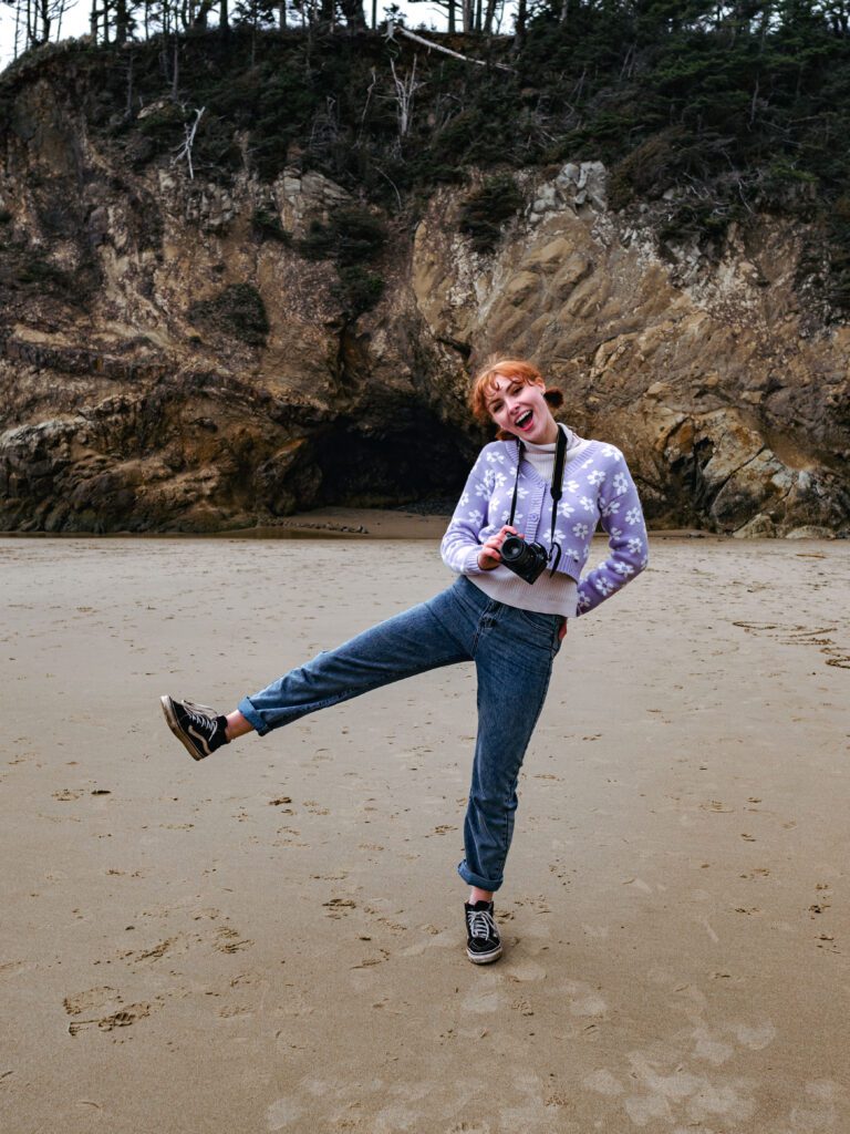 entrepreneur striking playful pose on sandy beach in front of rugged cliff