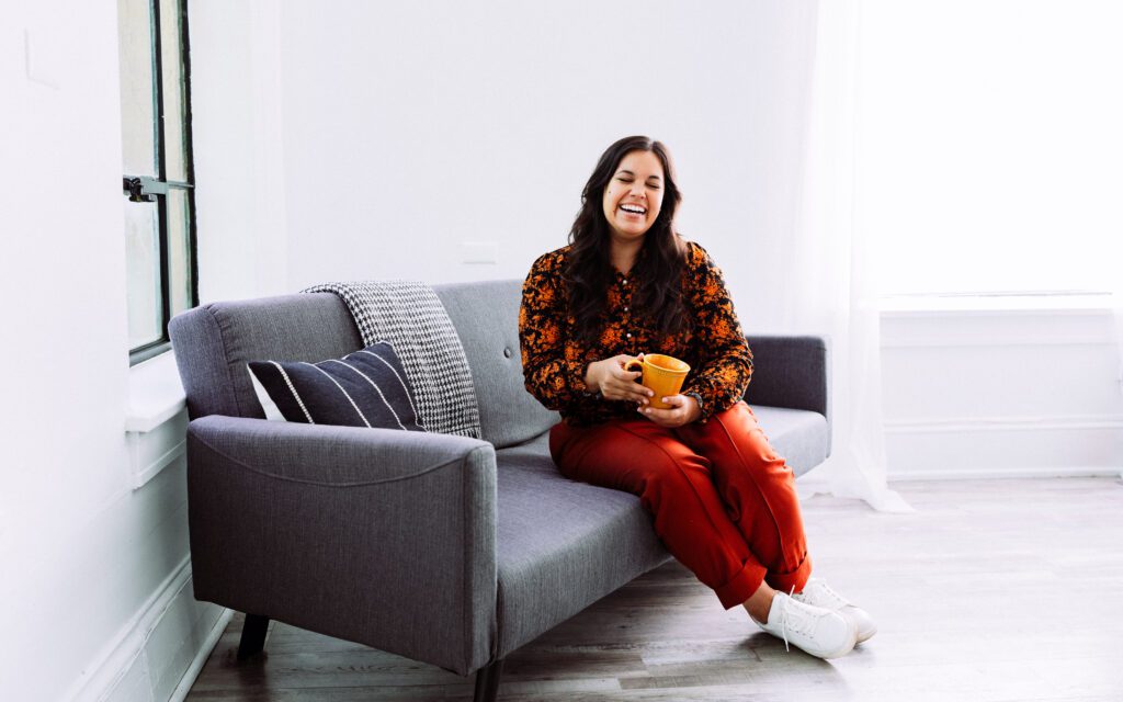 Full-body creative portrait of a music artist seated on a gray couch in a Portland studio branding session