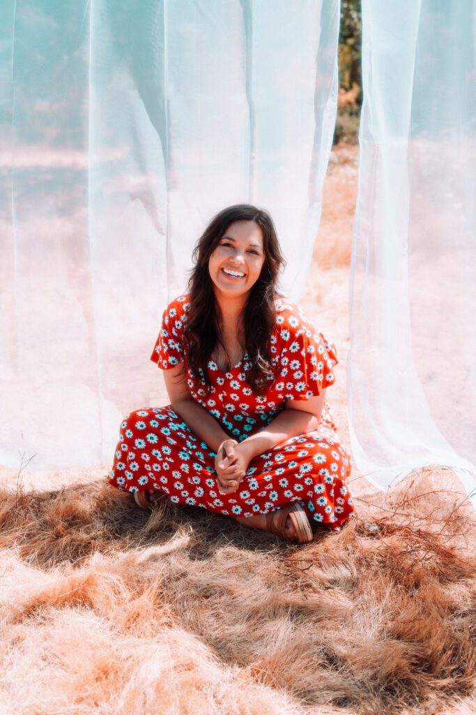 Musician in red floral dress sitting under sheer fabric during a personal branding photoshoot in Oregon