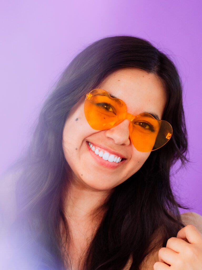 Close-up portrait of artist smiling in orange sunglasses during a colorful studio brand photoshoot
