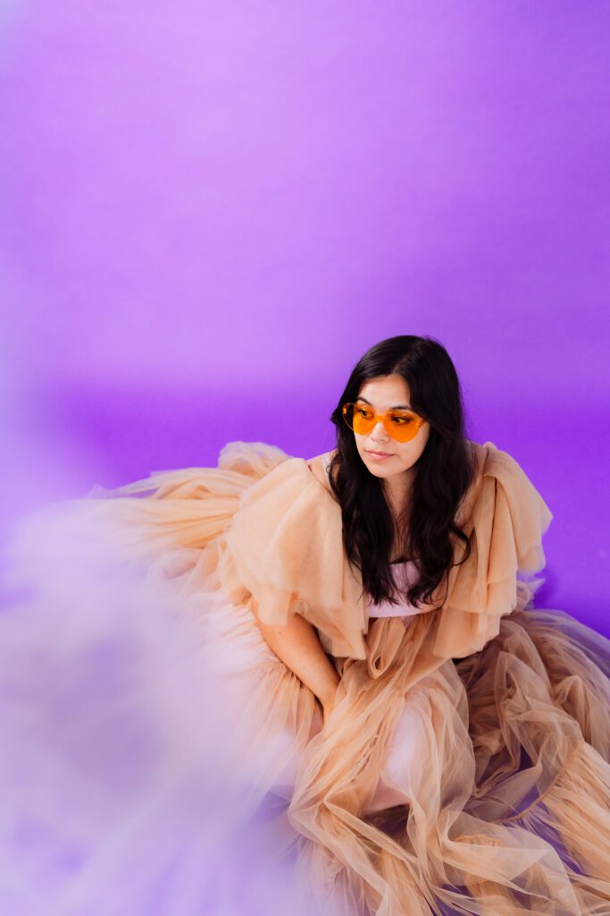 Singer wearing orange sunglasses and tulle dress in a bold monochrome setup for a creative brand session