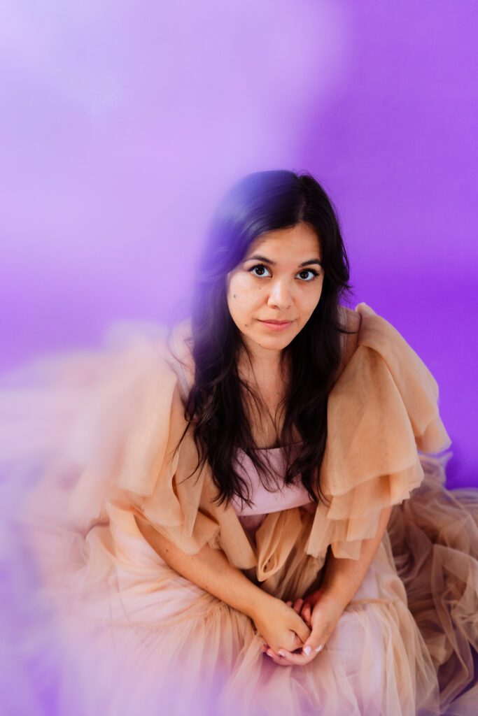 Soft haze portrait of a music artist in a layered gown against purple backdrop during a Portland studio shoot