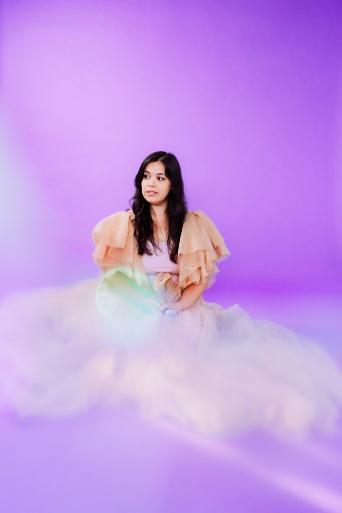 Musician seated in a peach tulle gown on a purple backdrop during a creative studio branding photoshoot