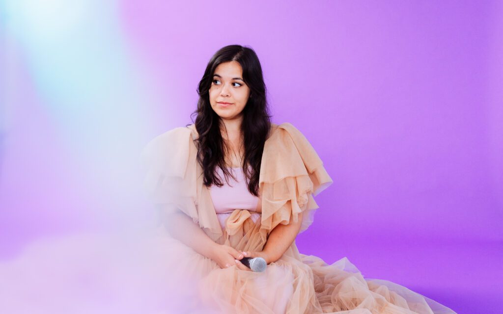 Female musician sits gracefully in a ruffled peach gown with a dreamy haze effect during her Portland brand photoshoot