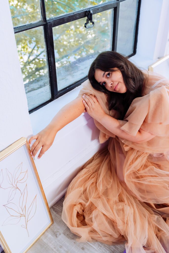 Musician in peach tulle gown smiling near the windows of a Portland studio during a relaxed brand session