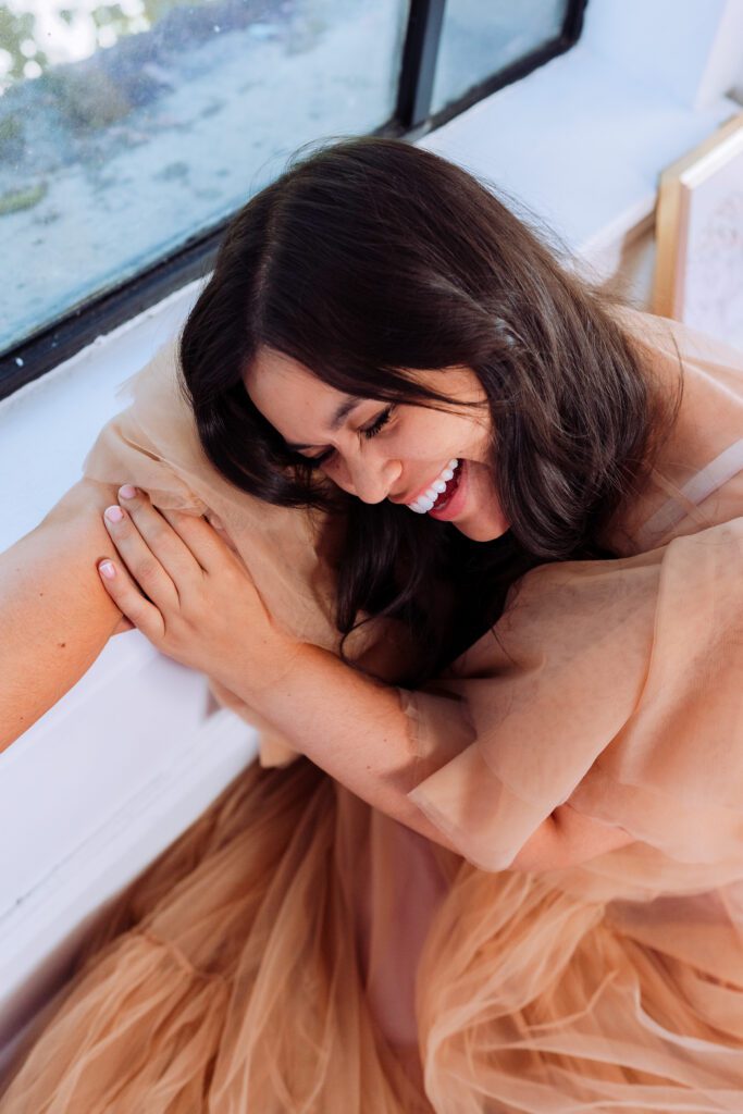 Artist smiling with arms folded in soft natural light by a window during a personal branding shoot