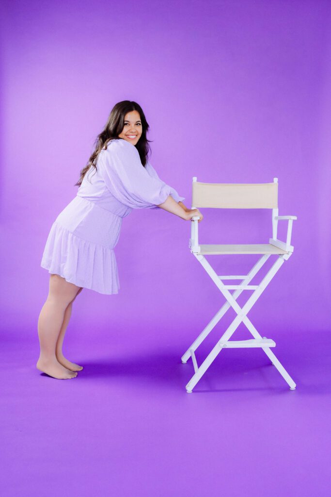 Artist playfully posing with a white chair against a bold purple backdrop during a Portland branding session