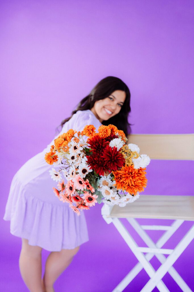 Musician in lilac dress holding a bouquet of orange and white flowers during a colorful studio branding shoot