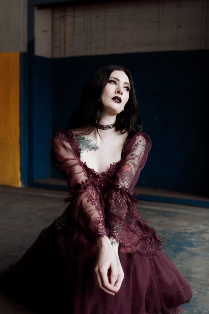 moody brand portrait of woman in burgundy gown seated in low light indoor space