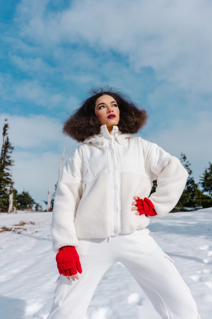Fashion-forward woman standing in snow with white coat and red gloves, looking away from camera—captured on location in Oregon mountains