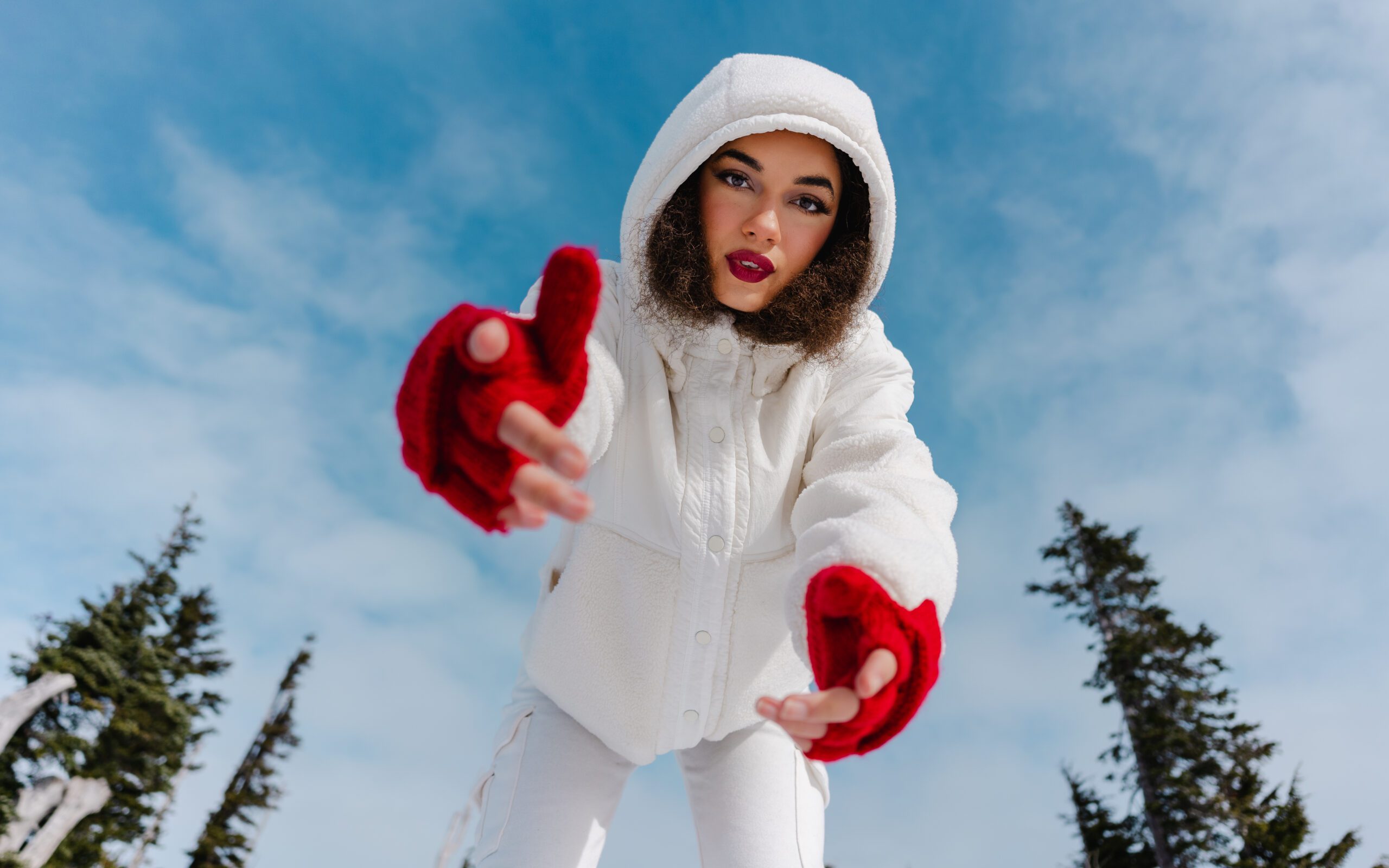 Woman in white coat with red mittens reaching toward camera, captured in playful perspective during a winter Outdoor Adventure session in Oregon