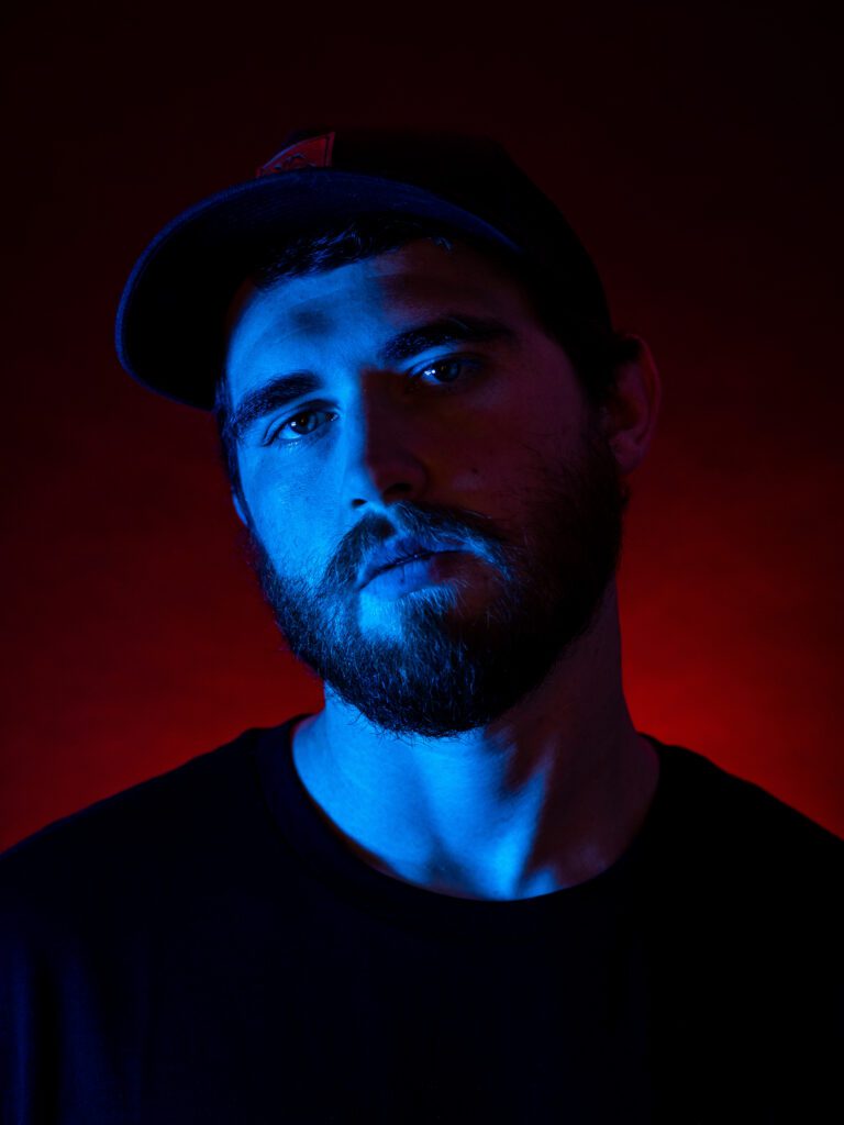 Moody brand headshot of man in dark t-shirt, dramatically lit with split blue and red gel lighting—captured during an expressive Studio Lab session by Mewphotovideo