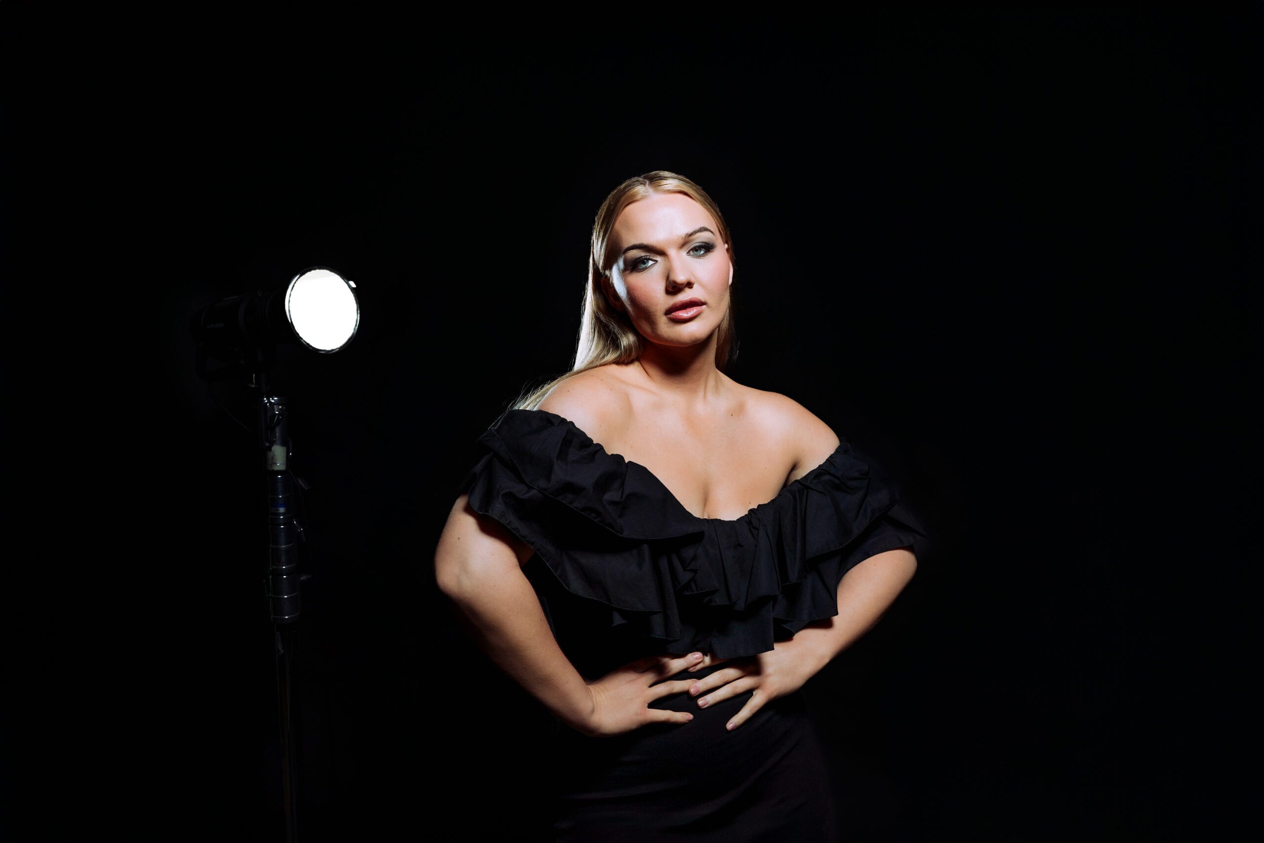 Creative studio portrait of a woman standing confidently in black attire under a spotlight, shot in a monochrome lighting setup at Cobalt Studios PDX