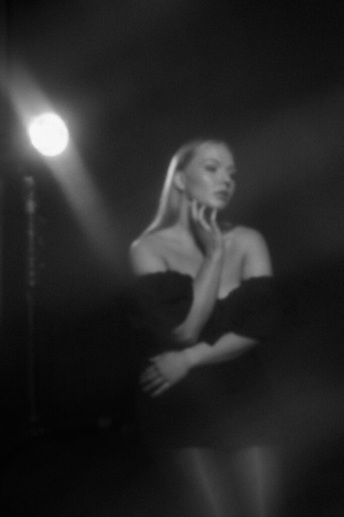 Editorial-style studio photo of a woman under a spotlight, surrounded by in-camera haze on a black background
