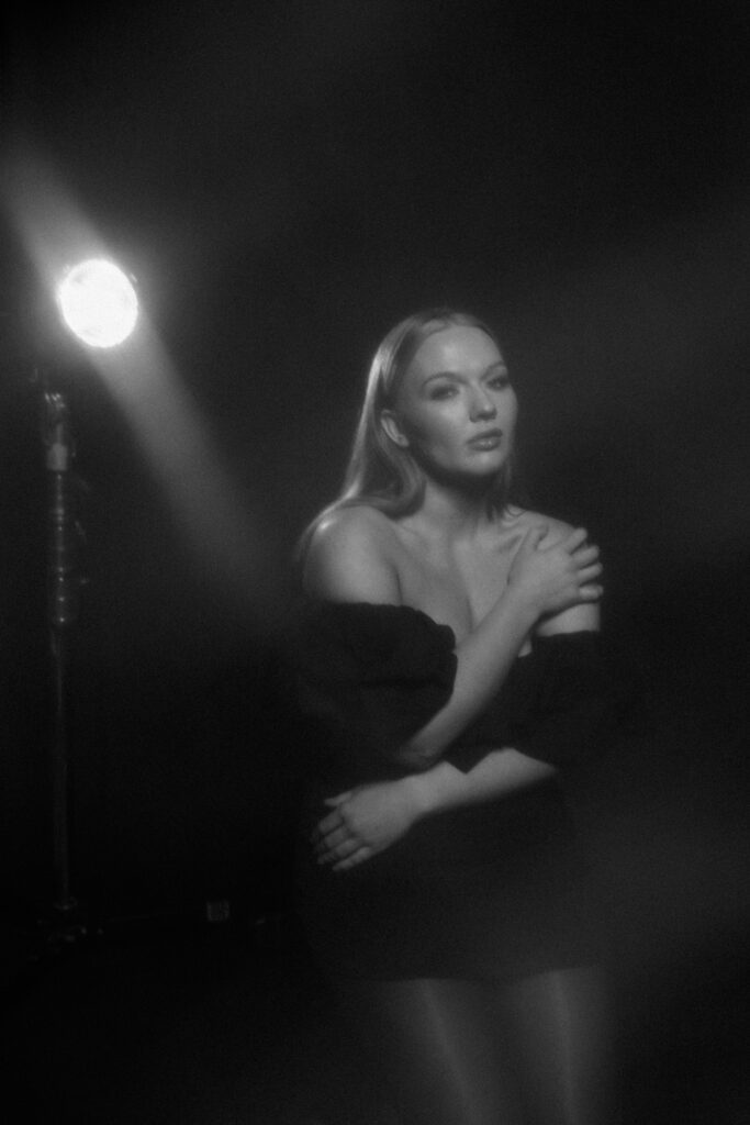 Portrait of a woman in off-shoulder black dress with soft cinematic haze, photographed in a dramatic monochrome studio setting