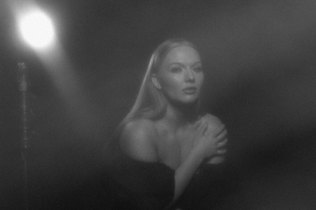 Creative black and white studio portrait of a woman in soft haze, lit by a spotlight, evoking classic film noir mood