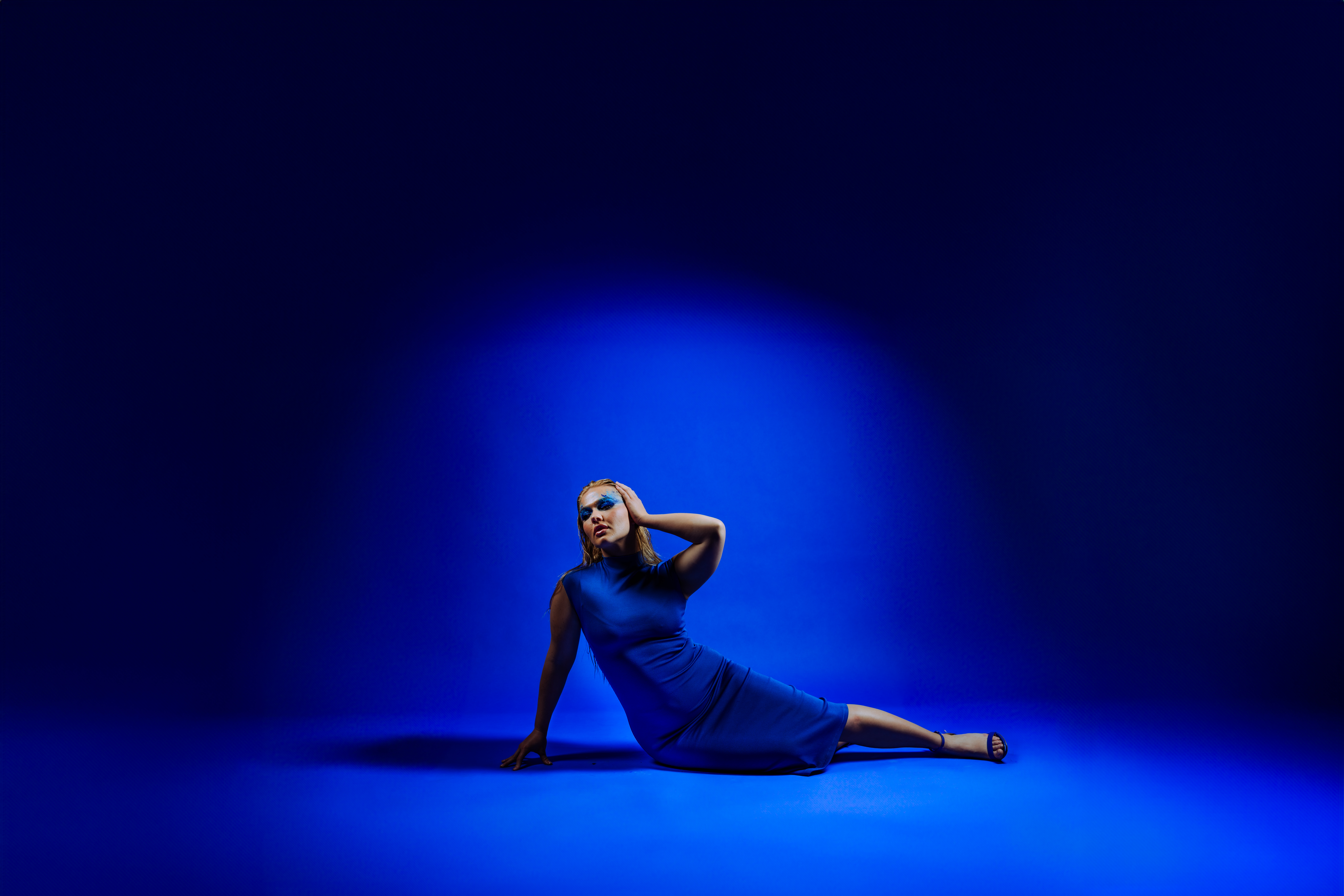 Client in a bold blue dress reclining on a matching blue studio backdrop, dramatically lit and styled to evoke clarity and confidence—featured brand portrait from a custom Speak Your Language session by Mewphotovideo