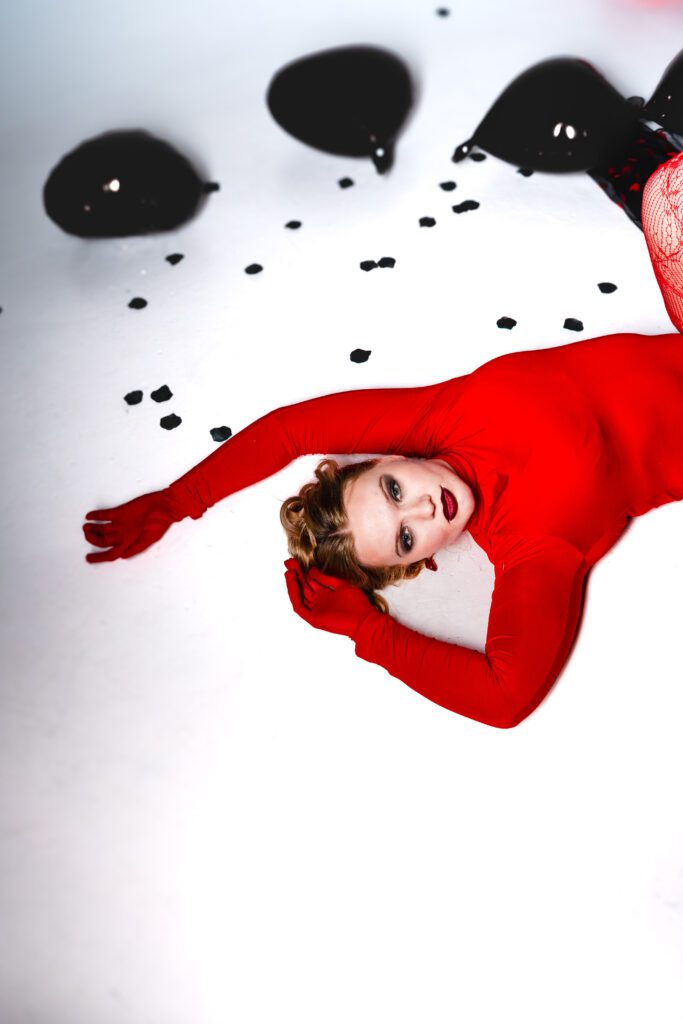 Client lying on the floor in red outfit surrounded by black petals, creating a powerful narrative image during a high-concept Studio Lab shoot