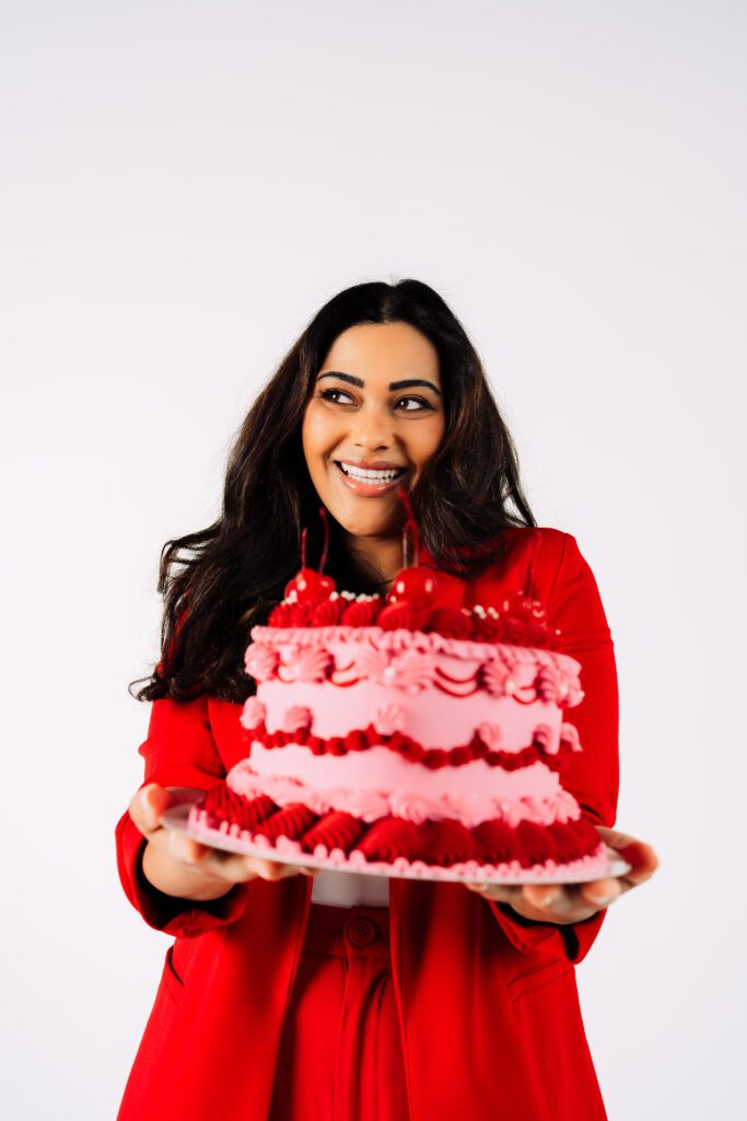 Woman beams while holding a pink and red cherry cake celebrating Rose & Salt Social’s second year in business, styled for a custom branding shoot