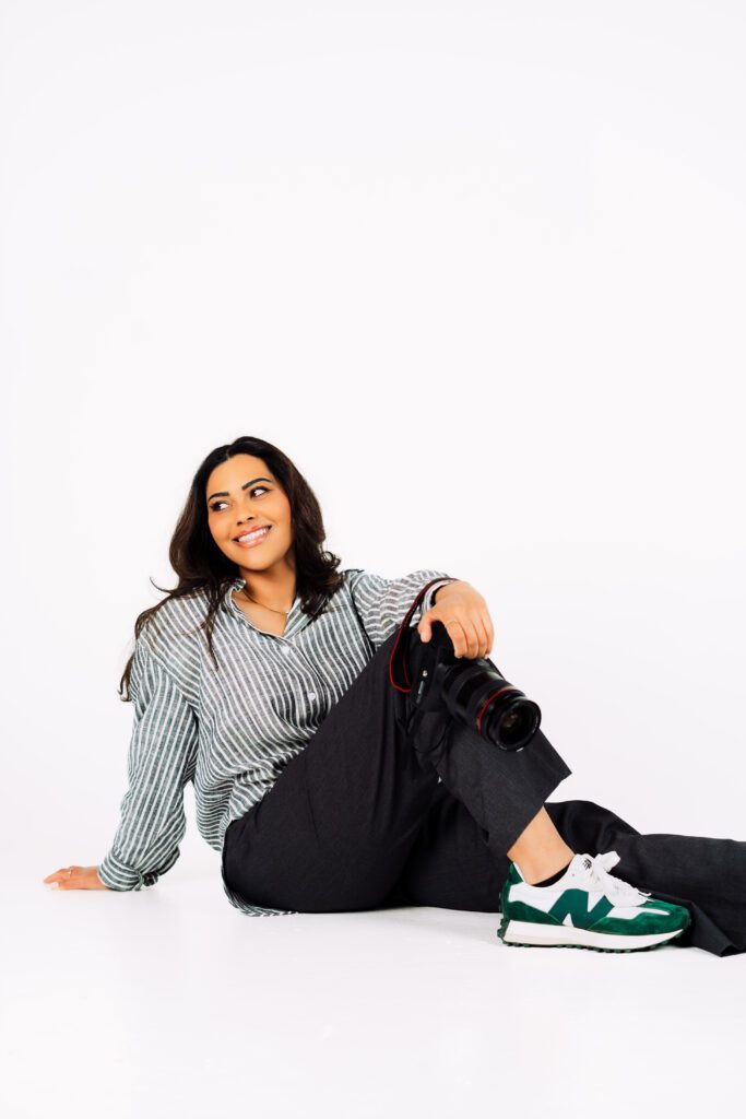 Creative Agency Founder of Rose & Salt Social sits comfortably on the floor in a striped shirt and sneakers, holding her camera during a creative brand session in Portland