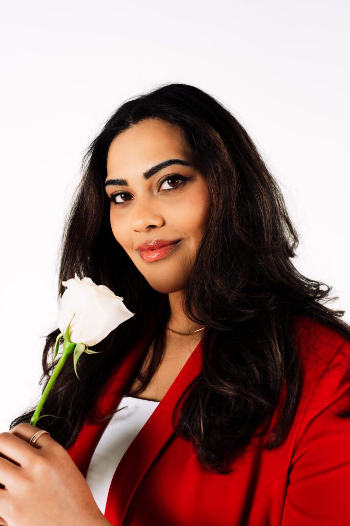 A confident close-up of female entrepreneur holding a white rose in her red suit during her Portland brand shoot with Mewphotovideo