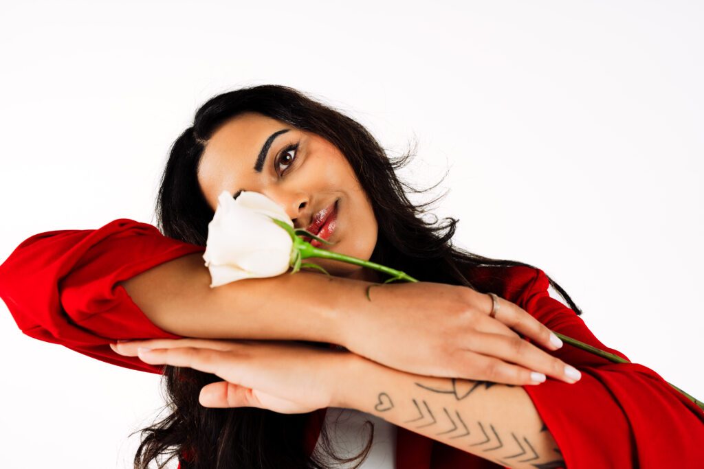 Close-up image of a woman in red gently holding a white rose with tattooed arms crossed—capturing tenderness and self-expression in a Speak Your Language session by Mewphotovideo