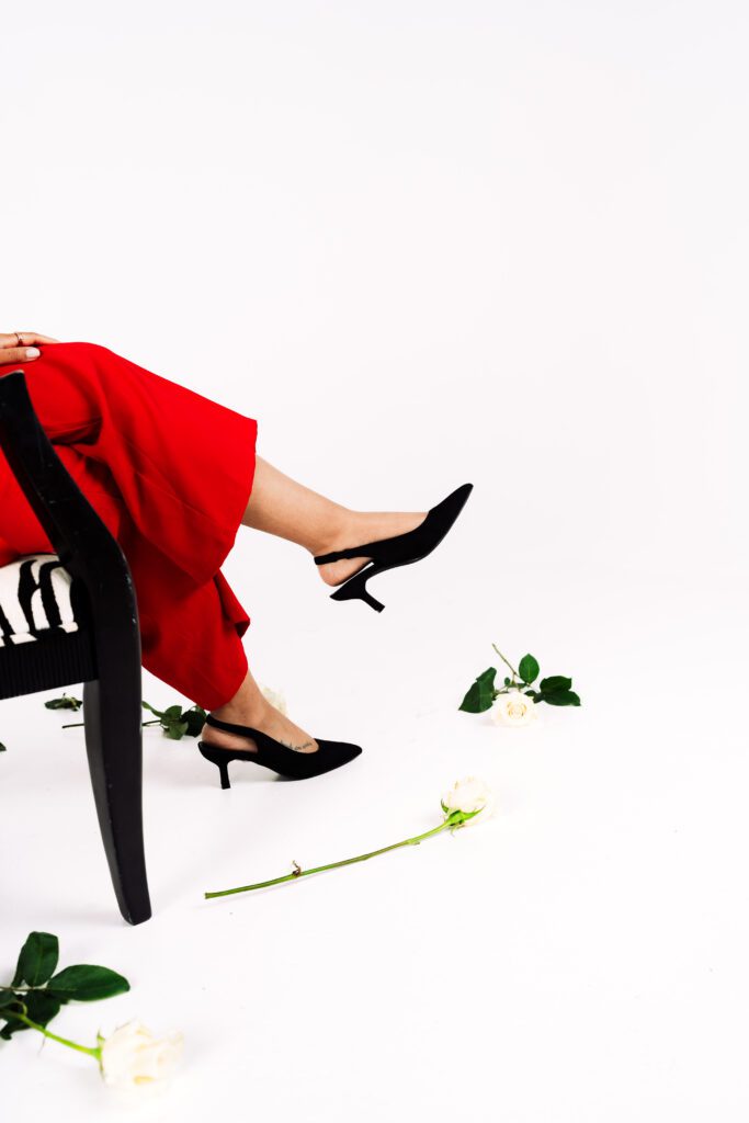 Founder of Rose & Salt Social sits on a stool with legs crossed as white roses decorate the studio floor in a playful branding photo