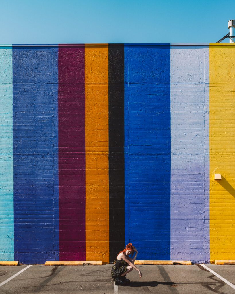 Center-framed subject seated in front of a large rainbow mural wall during an Outdoor Adventure photo session in Portland.